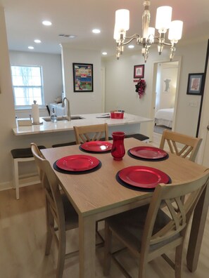 A dining area with a wooden table set for four, a chandelier, and a kitchen in the background. - Walk to the Grove! Perfect Game Day Condo! (Oxford)