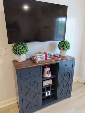 A dark blue cabinet with a TV mounted above it, two potted plants, a stack of books, and a decorative bell.