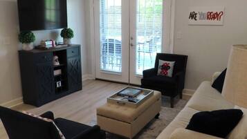Una sala de estar con sofá, sillón, reposapiés y un televisor de pantalla plana montado en la pared.