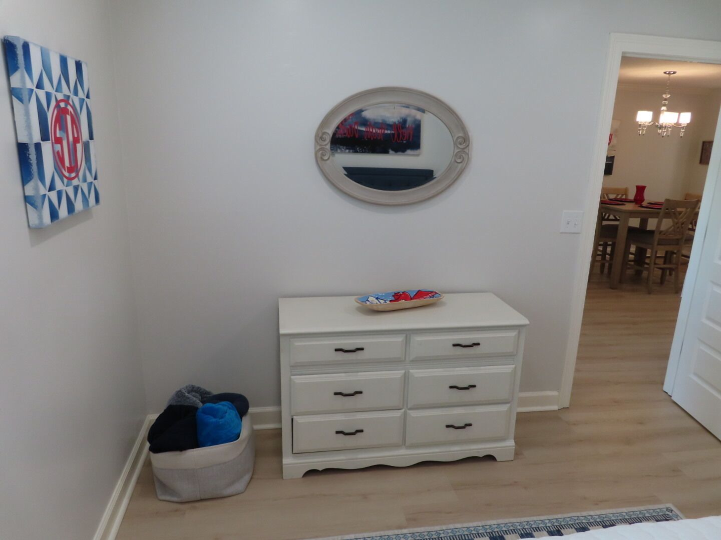A hallway with a white dresser, a round mirror, and a wall art piece.