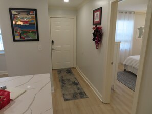 A hallway with a white door, a framed poster on the wall, and a small rug on the floor.