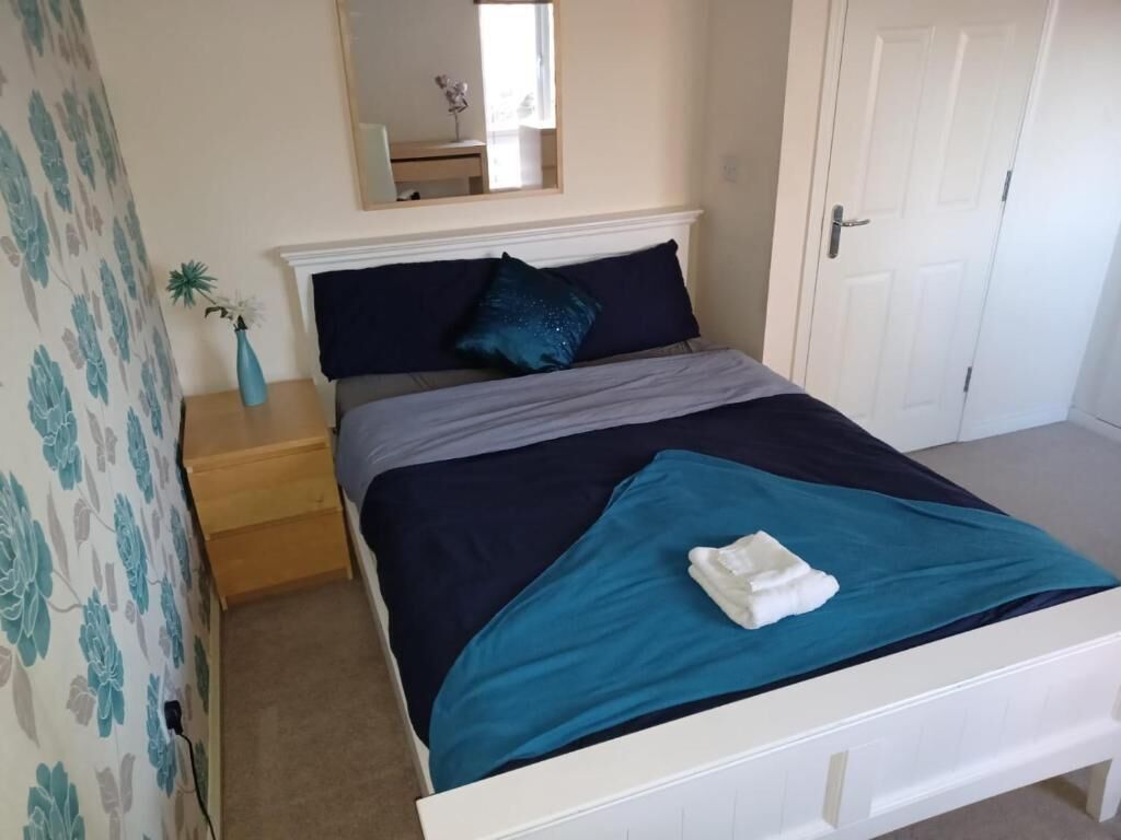 A bedroom with a bed, a nightstand, a mirror, and a door.