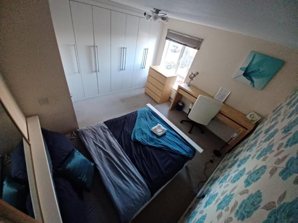 A bedroom with a bed, a desk, a wardrobe, and a window.
