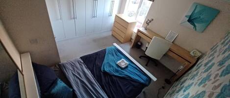 A bedroom with a bed, a desk, a wardrobe, and a window.