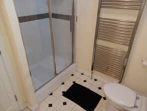 Un baño con inodoro, ducha con puerta de vidrio y barra para toallas.