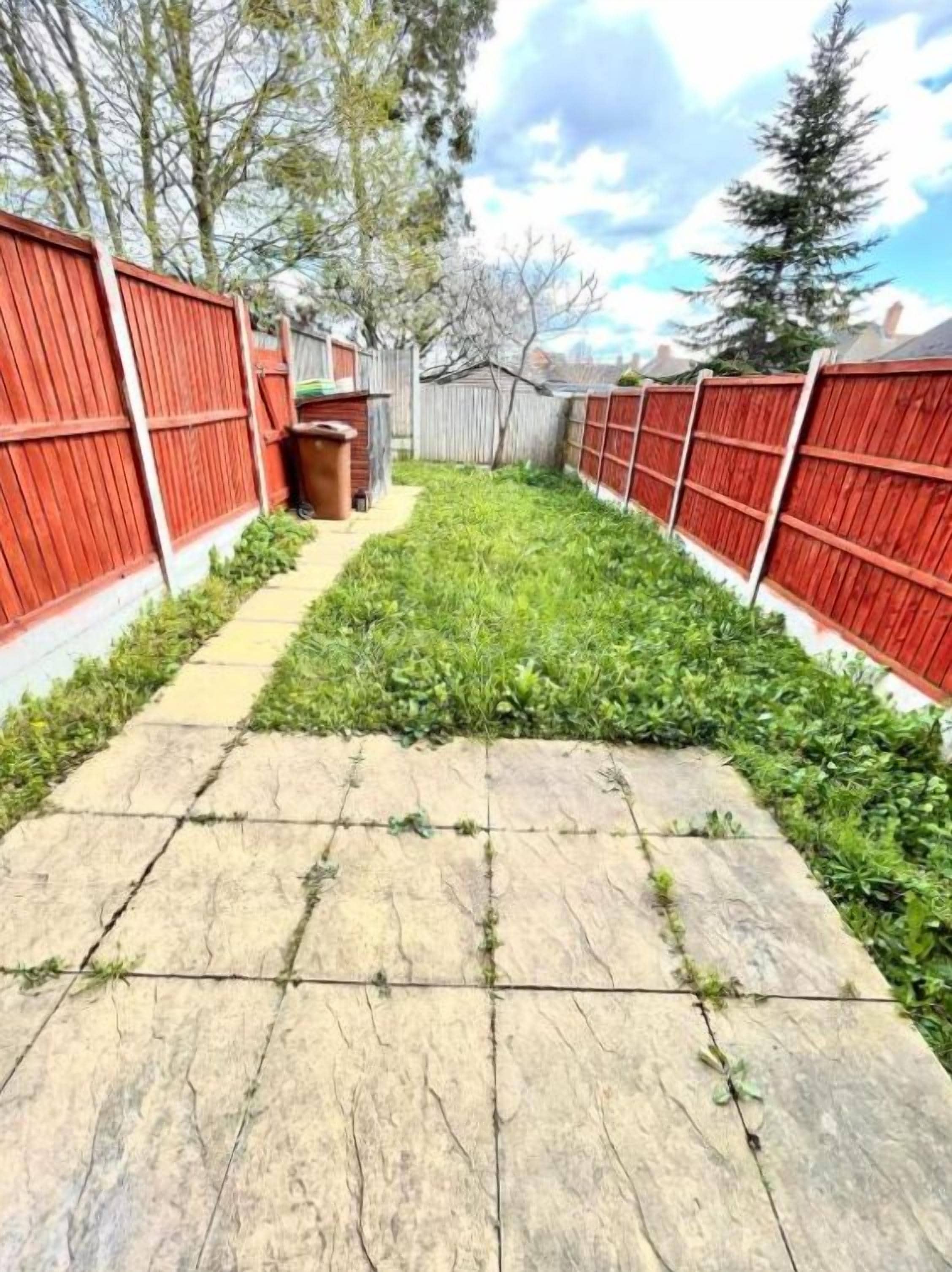 Un patio trasero con un camino de piedra, una valla de madera y un cobertizo pequeño.