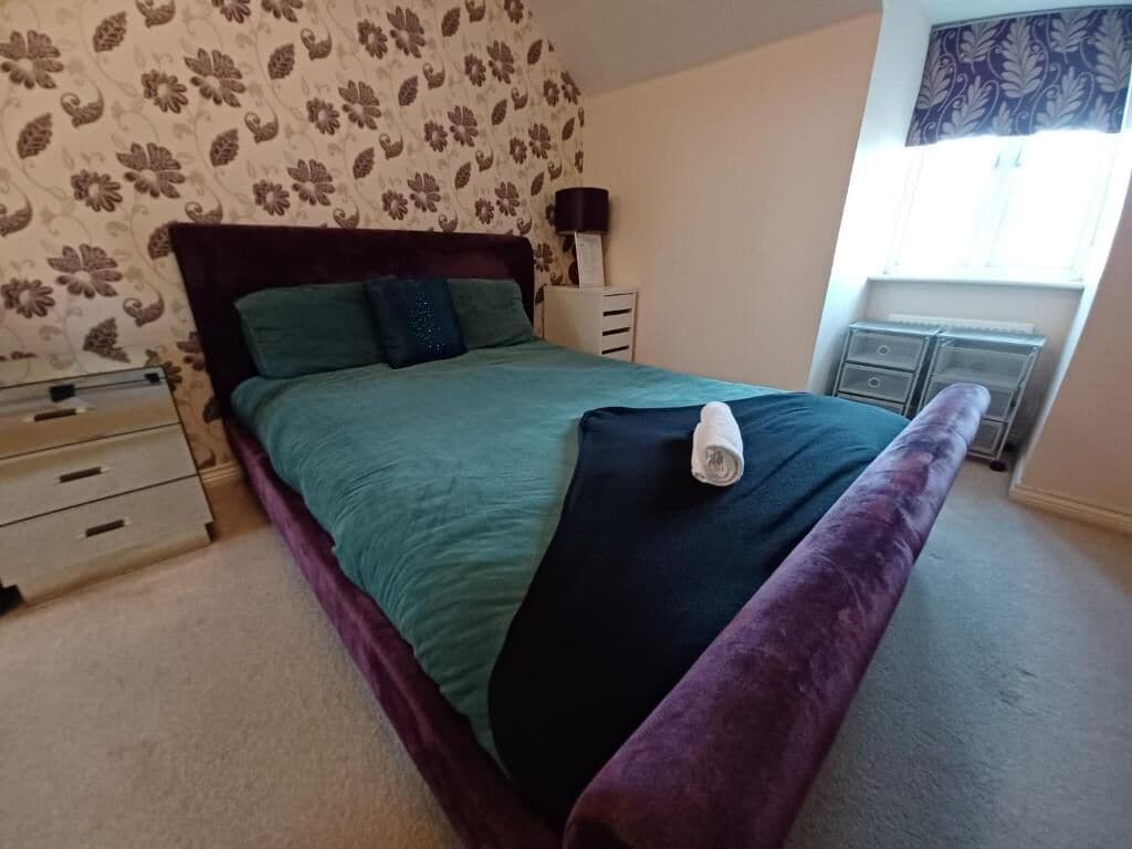 A bedroom with a bed, a nightstand, a dresser, and a window with curtains.