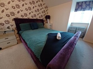 A bedroom with a bed, a nightstand, a dresser, and a window with curtains.