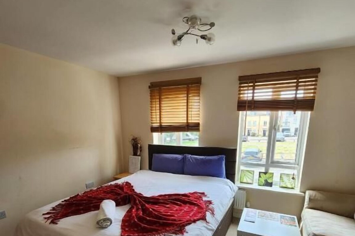 A bedroom with a bed, a bedside table, a chair, a window with blinds, and a ceiling fan.