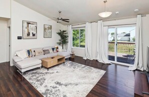 A modern living room with a white sofa, a coffee table, and a large window with curtains. - Des Moines Ranch near Altoona | Fenced Yard, 3BR (Des Moines)