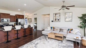 A modern living space with a kitchen, bar stools, a sofa, and a ceiling fan. - Des Moines Ranch Retreat (Des Moines)