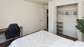 A bedroom with a bed, a desk, a chair, a closet with hangers, and a potted plant. - Des Moines Ranch Retreat (Des Moines)