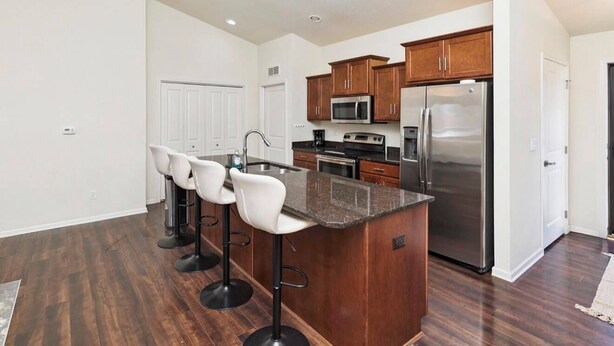 A modern kitchen with a central island, bar stools, stainless steel appliances, and wooden cabinets. - Des Moines Ranch Retreat (Des Moines)