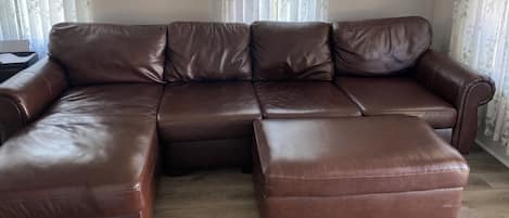 Ein braunes, ledernes Ecksofa in einem Wohnzimmer mit blumigen Vorhängen und zwei Wanddekorationen.