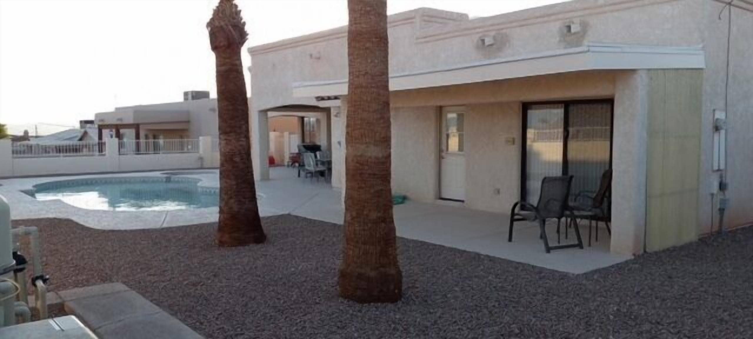 A pool area with palm trees, a covered seating area, and a building with a flat roof.