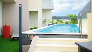 Uma área moderna da piscina ao ar livre com vista clara para o céu, um conjunto de degraus que levam a uma varanda e um pequeno jardim com um vaso vermelho.