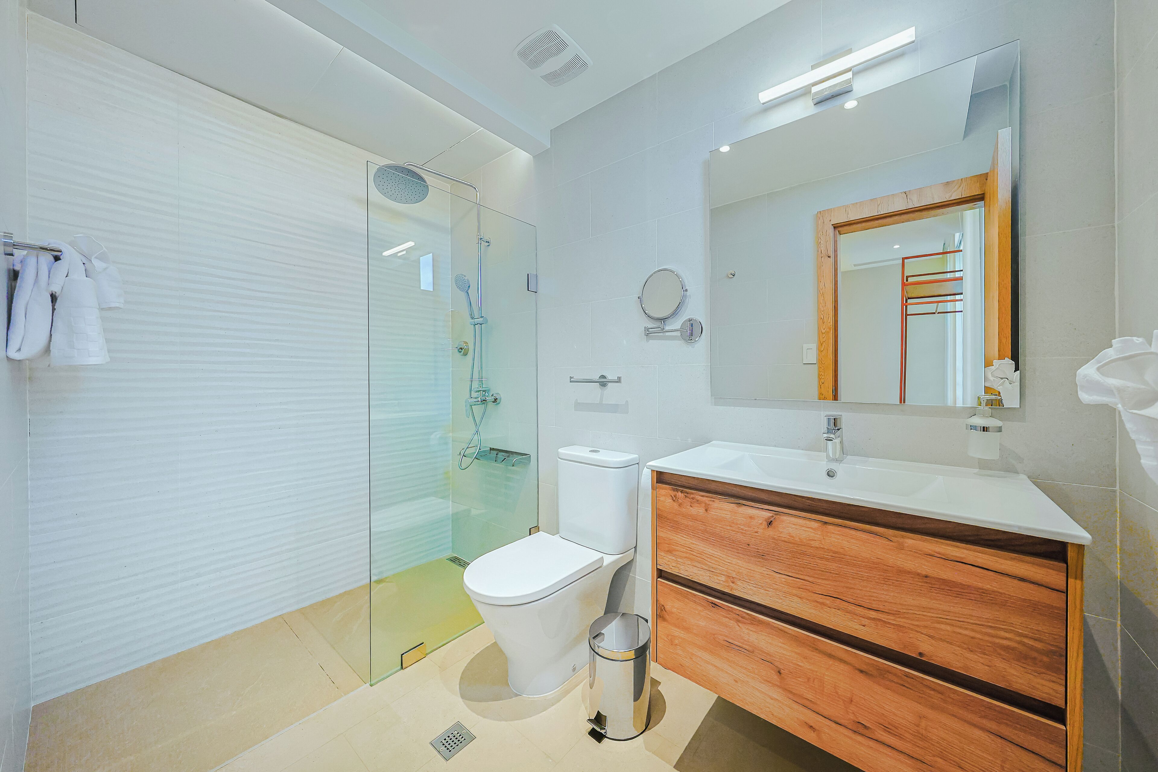 A modern bathroom with a glass shower enclosure, a toilet, a sink with a wooden vanity, and a mirror.