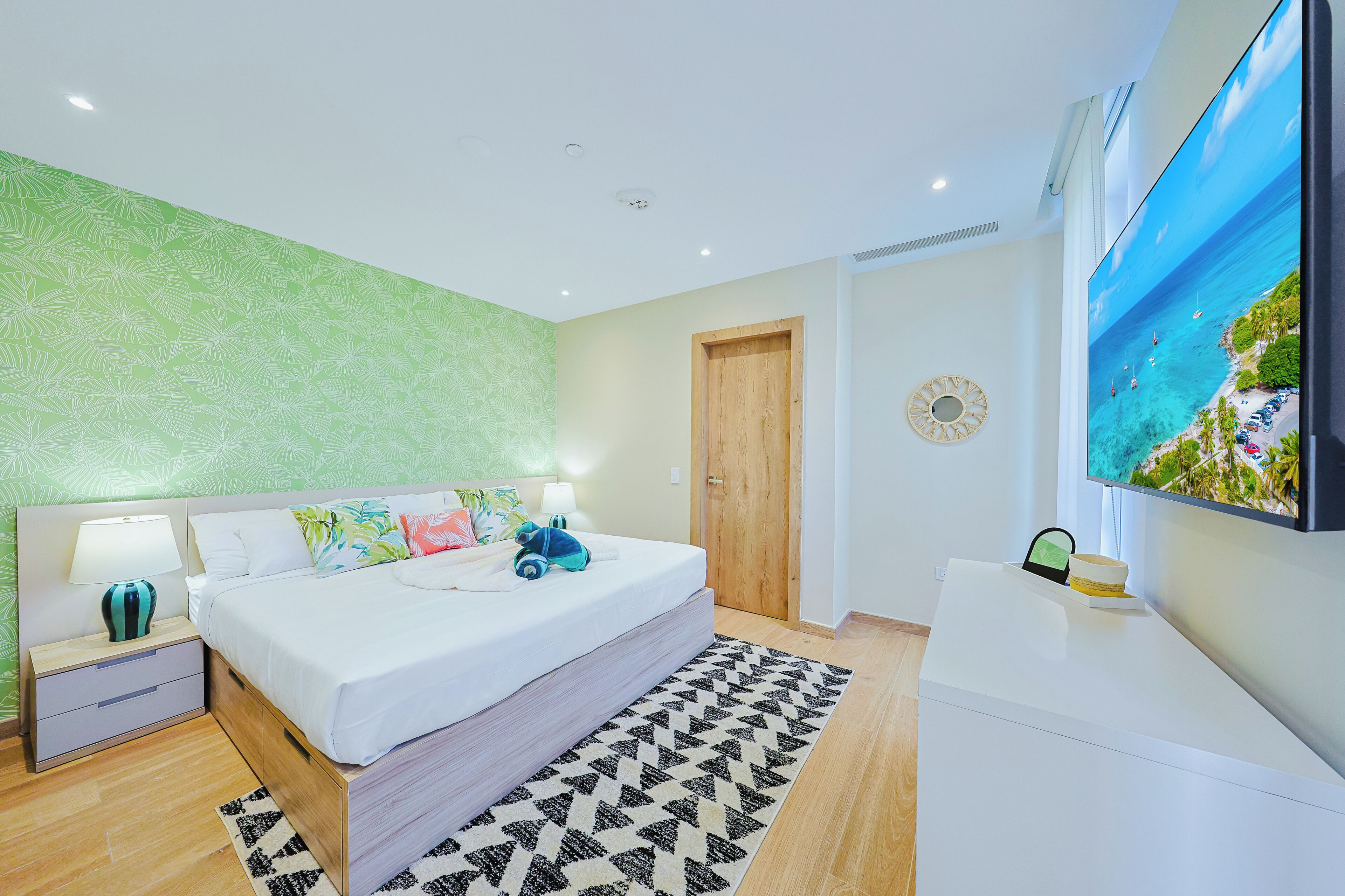 A modern bedroom with a bed, bedside tables, a TV, and a view of the sea.