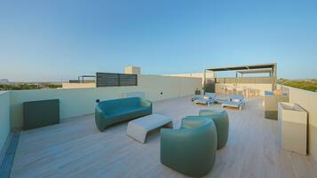 A rooftop terrace with modern furniture, a pergola, and a view of the cityscape.