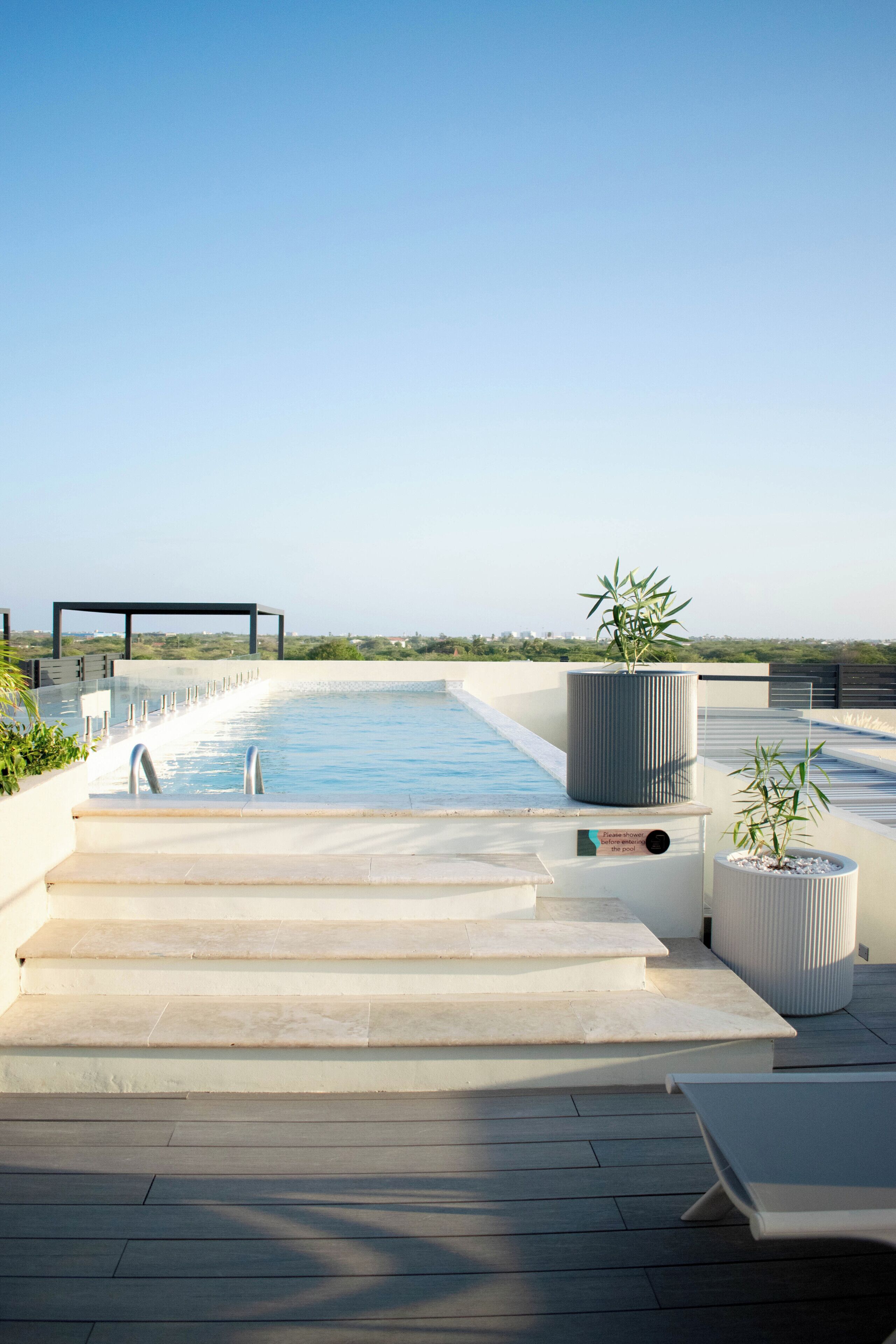 A rooftop pool with clear blue water, steps leading down to the pool, and a view of the city skyline in the background.