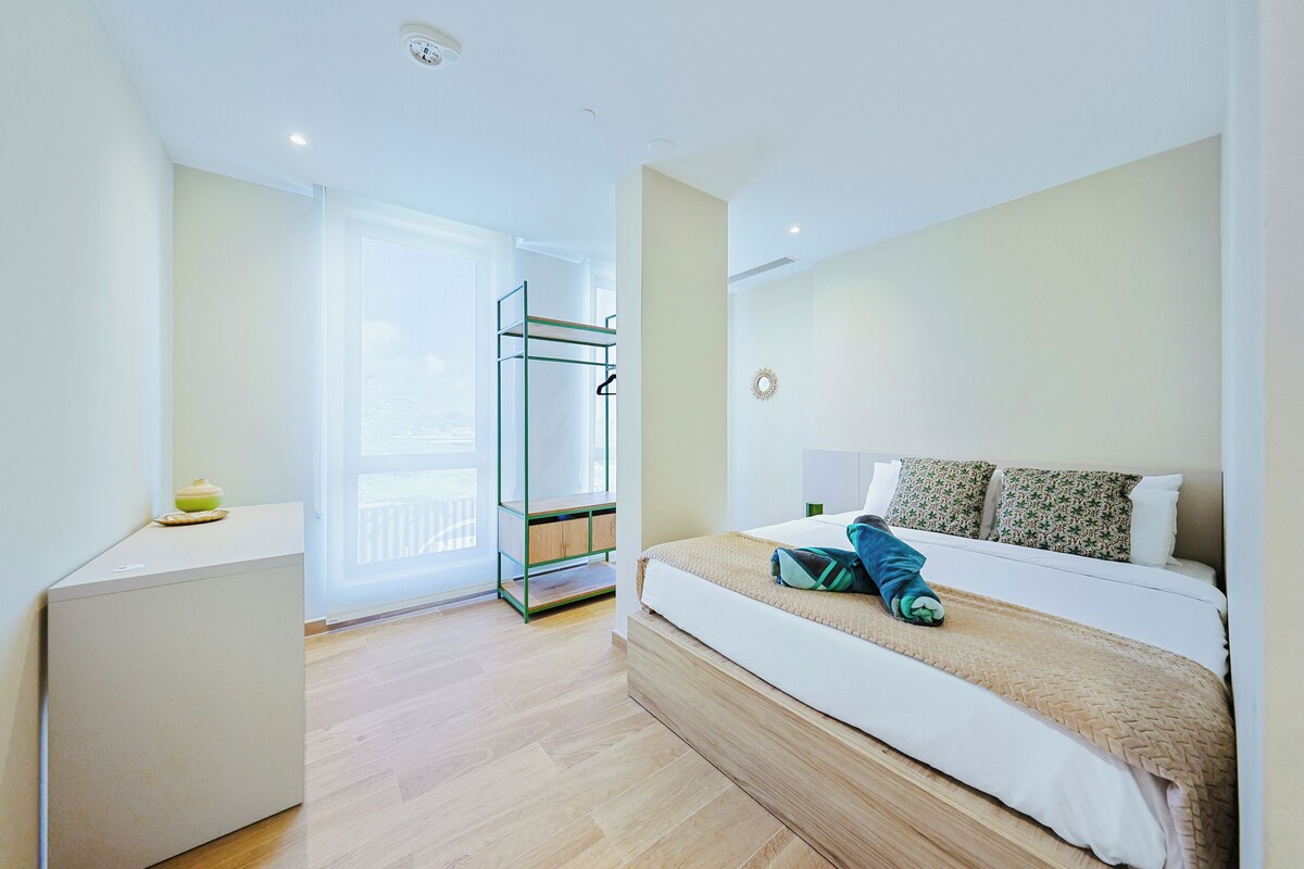 A hotel room with a bed, a bedside table, a wardrobe, and a view of the outside.