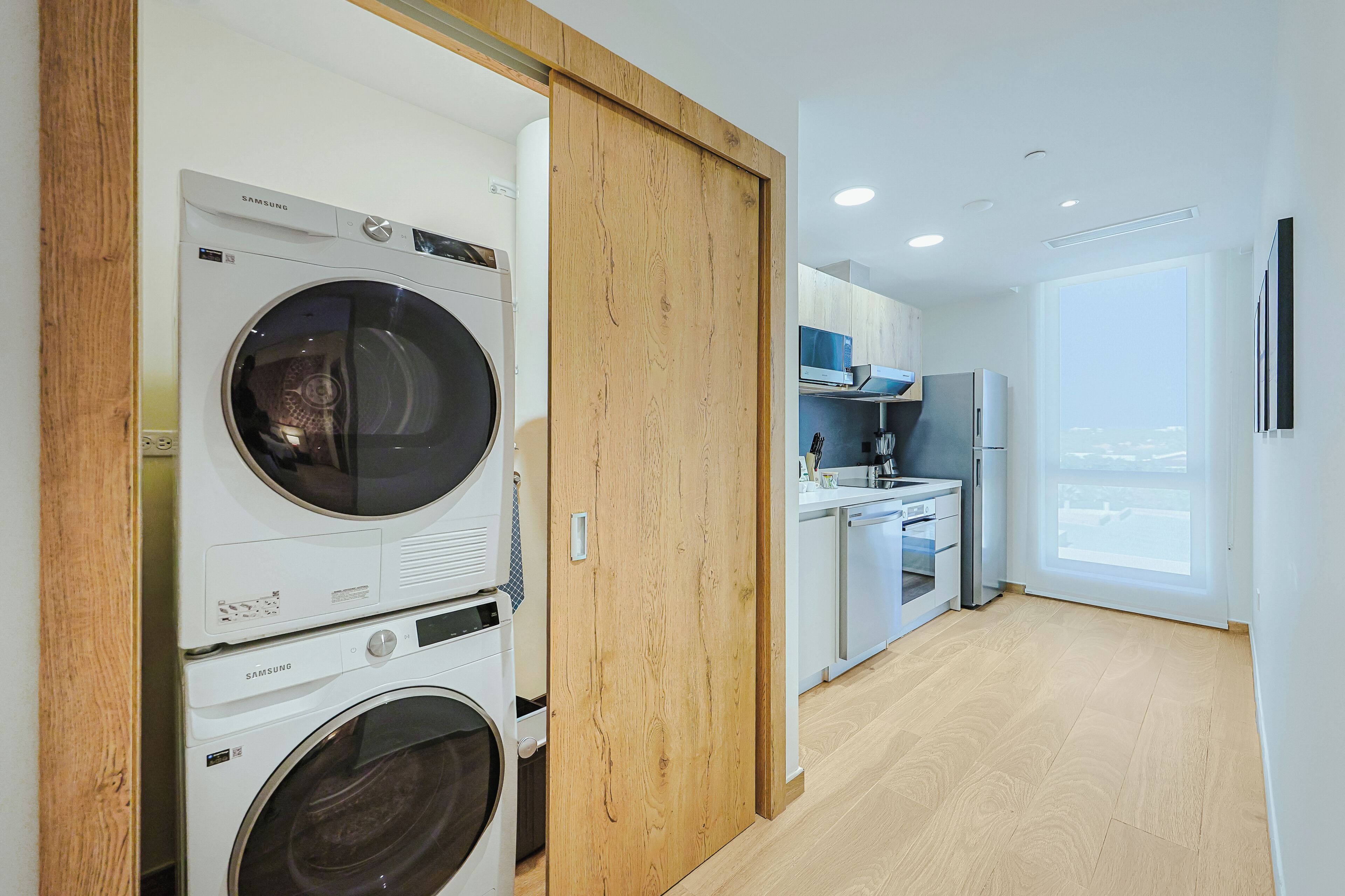 A modern kitchen with built-in appliances, a wooden door, and a view of the outdoors.