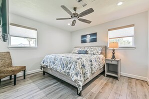 A bedroom with a bed, a ceiling fan, a nightstand with a lamp, and two windows. - Blue Haven | Canal-front retreat | Boat-Slip (Galveston)