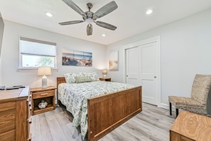Un dormitorio con cama, mesita de noche, lámpara, silla y ventilador de techo.