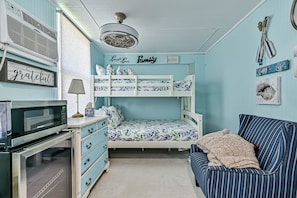 A room with bunk beds, a microwave, a dresser, a sofa, and a ceiling fan. - Blue Haven | Canal-front retreat | Boat-Slip (Galveston)