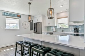 A modern kitchen with a large island, bar stools, stainless steel appliances, and pendant lighting. - Blue Haven | Canal-front retreat | Boat-Slip (Galveston)