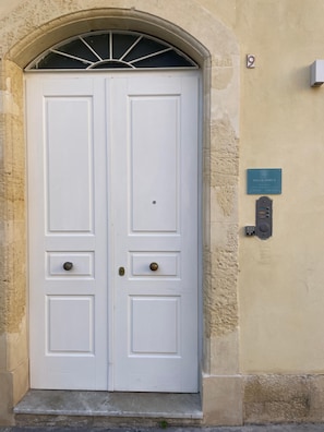 Une porte double blanche, surmontée d’une grille métallique, dotée d’un clavier pour le code et d’une plaque fixée au mur, sur le côté droit.