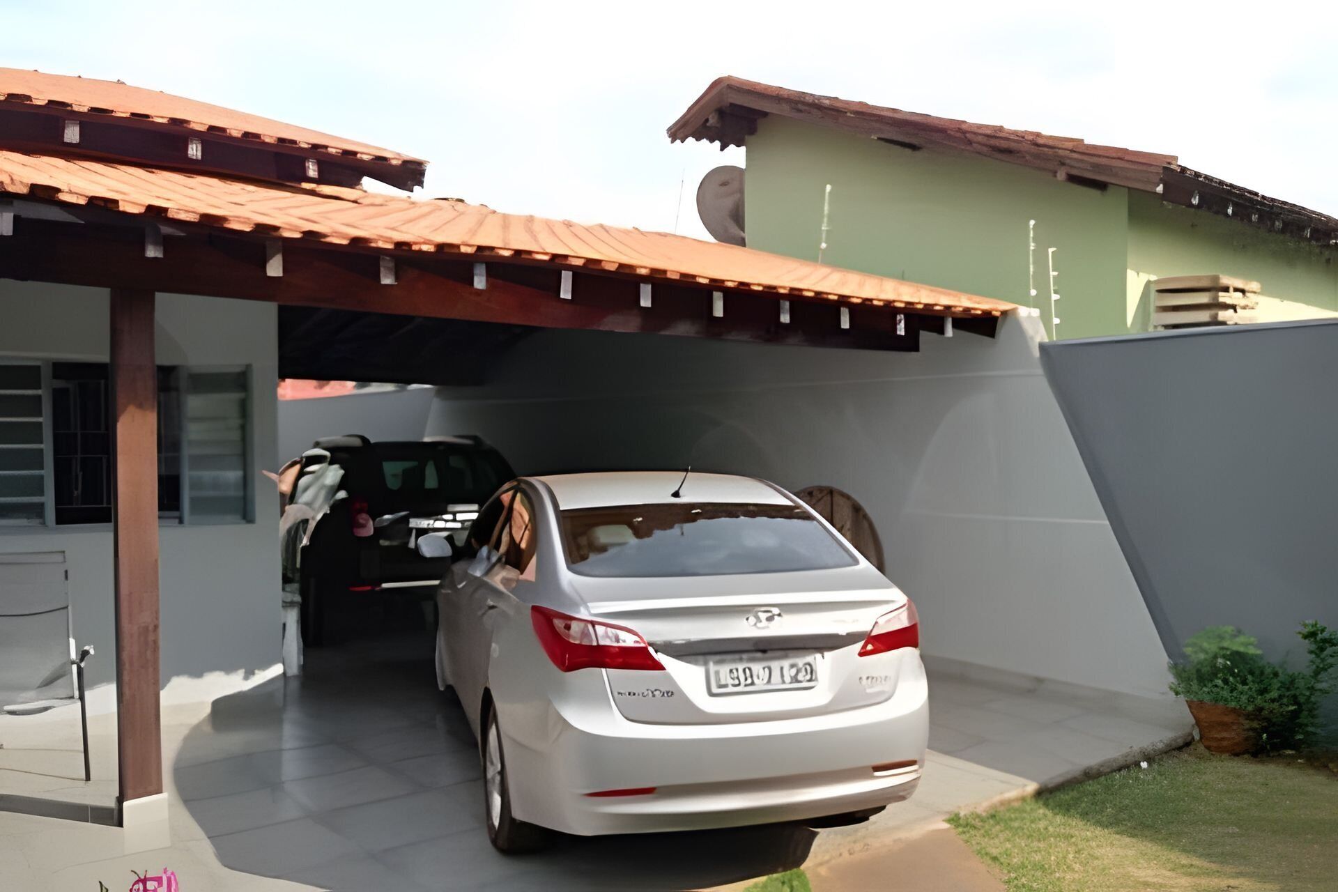 A white car parked under a covered area with a green wall and a brown roof.
