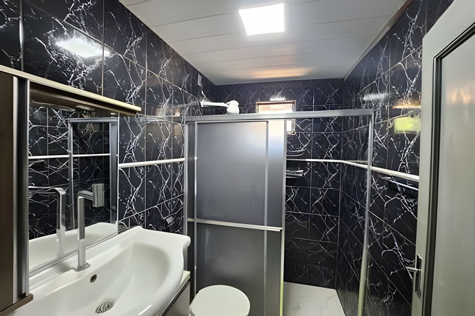 A bathroom with a white sink, a mirror, a toilet, and a shower enclosure.