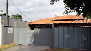 A fenced property with a metal gate, a paved driveway, and a building with a red roof. - DOURADOS GUEST FLAT (Dourados)