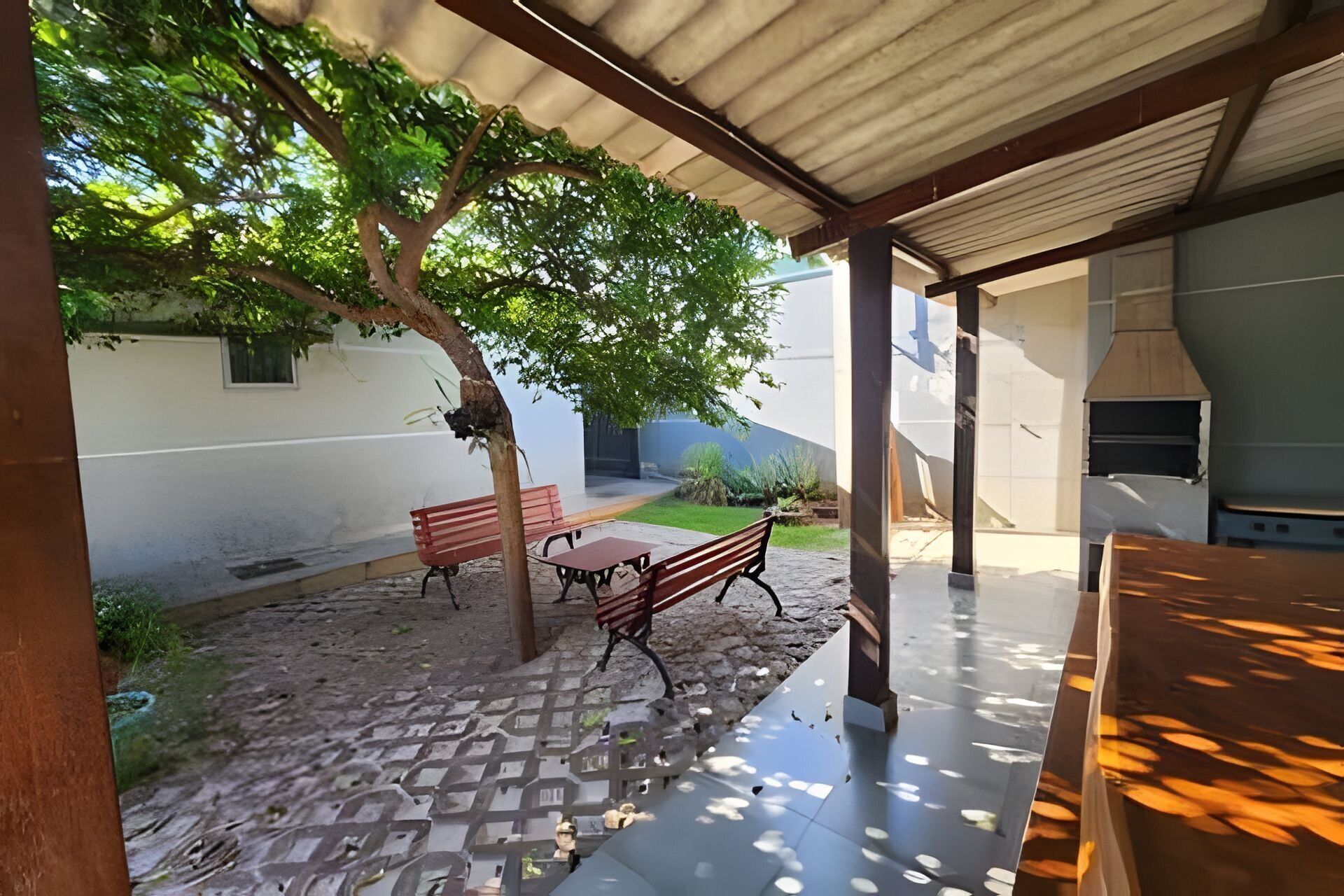 An outdoor patio area with a covered seating area, a tree, and a barbecue grill.