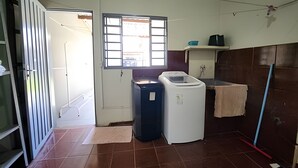A compact kitchen with a window, a washing machine, and a sink. - DOURADOS GUEST FLAT (Dourados)
