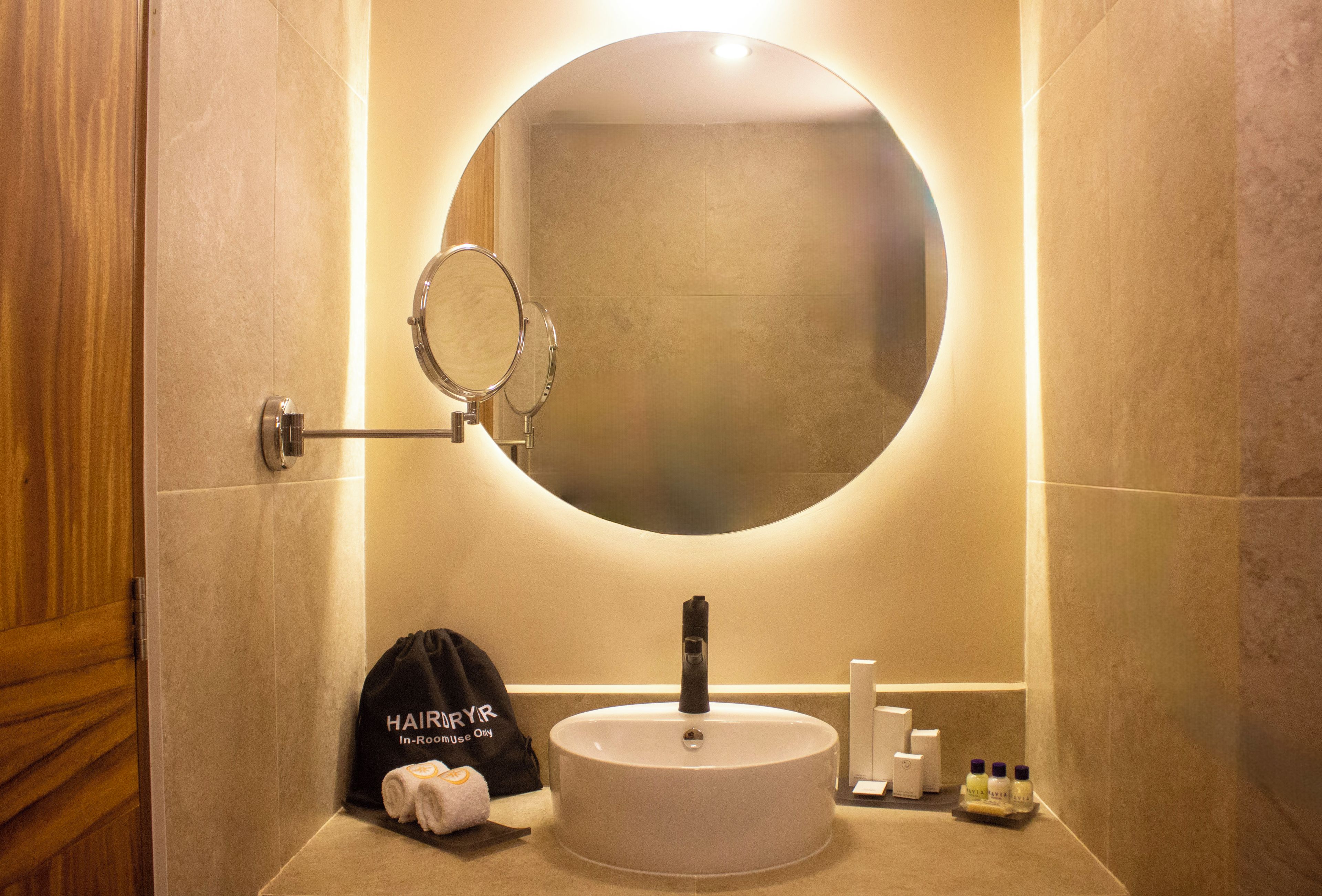 Un baño con un espejo redondo, un lavabo, artículos de aseo y una toalla.