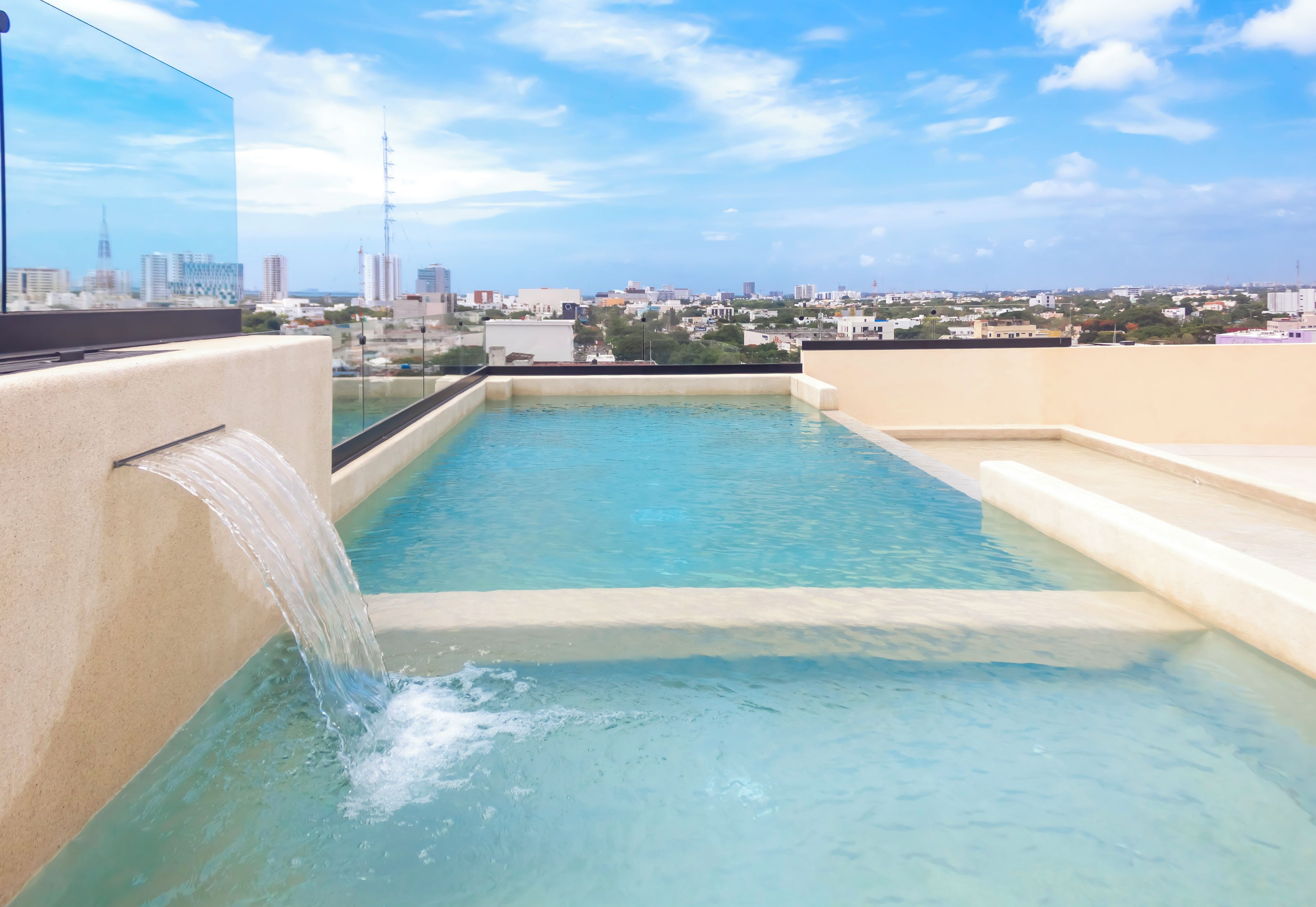 A rooftop swimming pool with a waterfall feature, surrounded by a cityscape view.