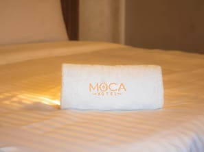 A neatly made bed with a folded towel on it, featuring the text 'MOCA HOTEL'. - Hotel Moca (Cancún)