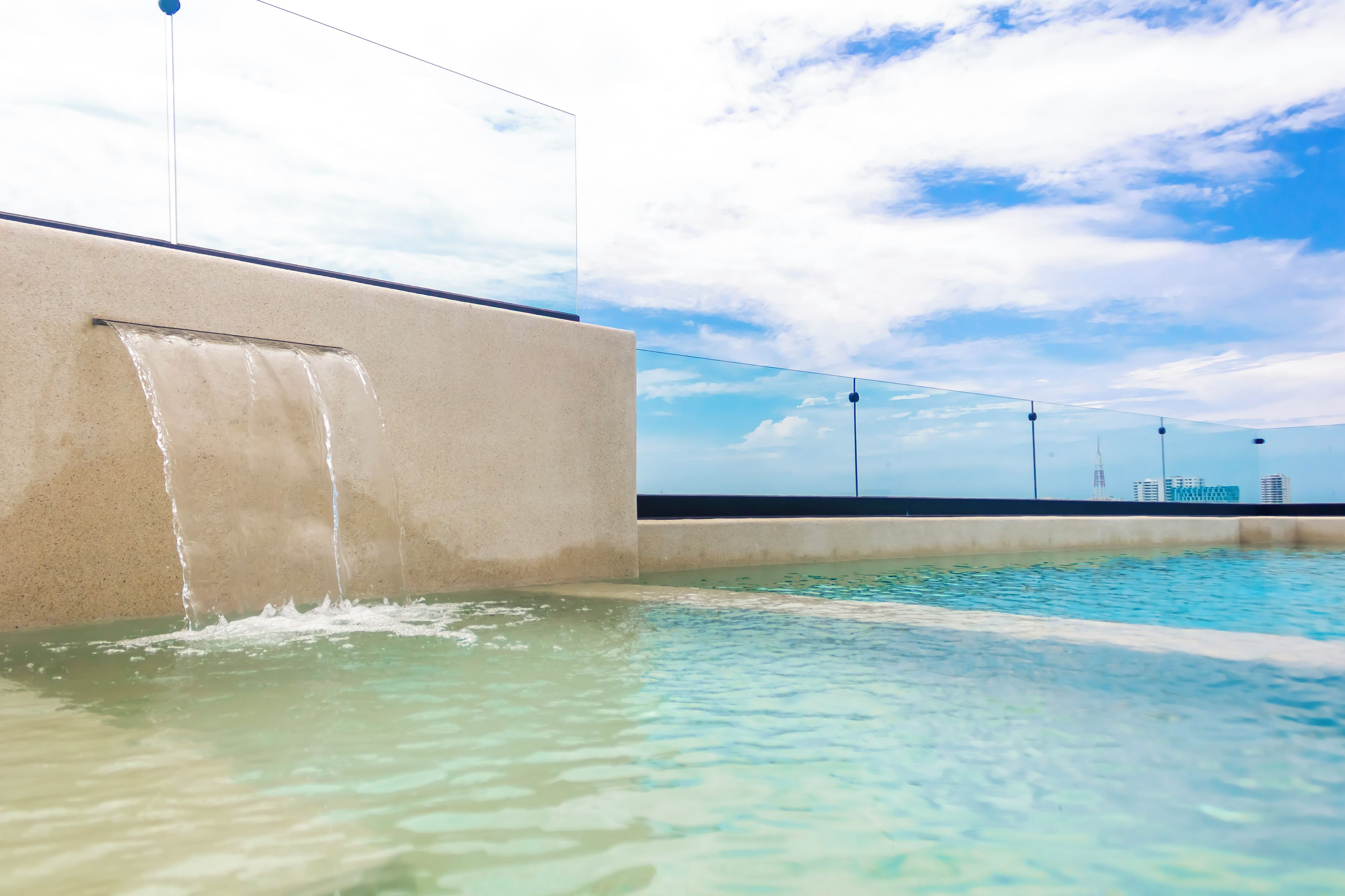 A swimming pool with clear water, a concrete wall, and a view of buildings in the distance.