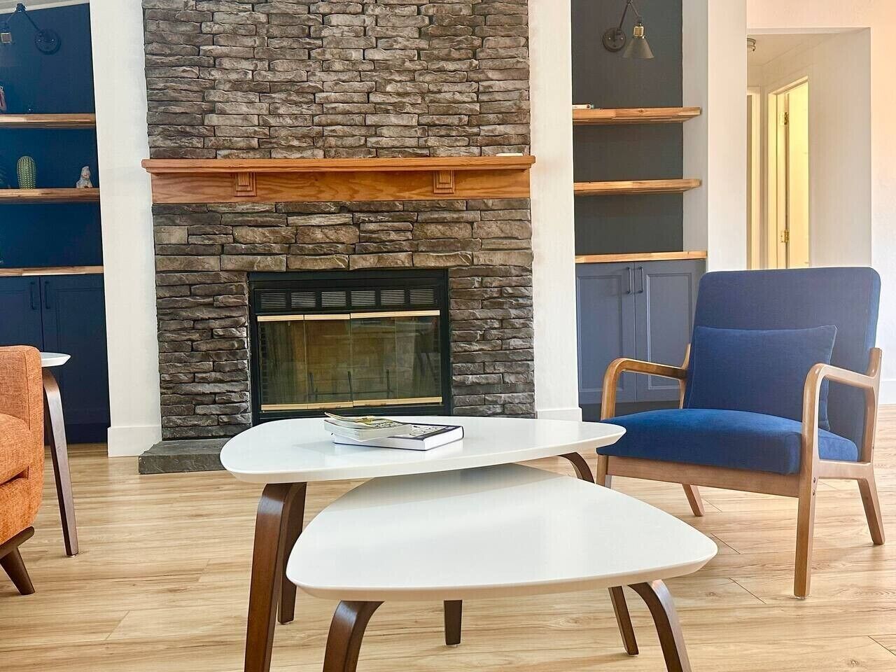 A living room with a stone fireplace, a blue armchair, and a white coffee table.