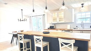 Een keuken met een centraal eiland, barkrukken, hanglampen en een raam dat natuurlijk licht binnenlaat.