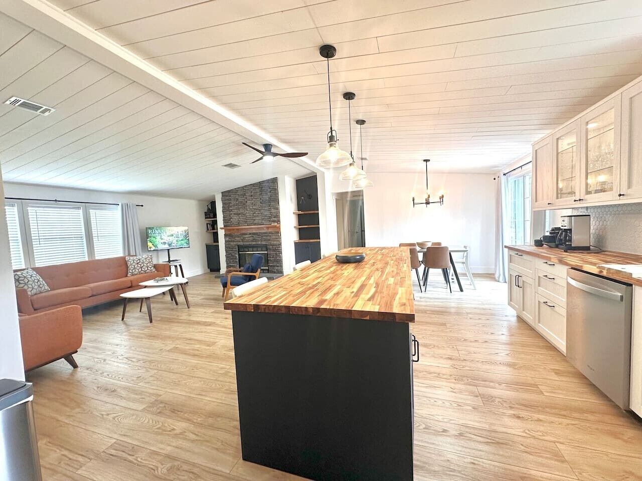 A modern kitchen with a wooden island, a dining area with chairs, and a living room with a sofa and TV.