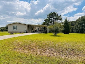 A single-story house with a covered porch, surrounded by a grassy field and trees. - The Blue Pony - 5 Miles to WEC! 10 Miles to HITS! (Ocala)