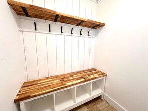 Eine Holzbank mit querverlaufenden Latten und eine weiße Wand mit einem Kleiderhaken darüber.