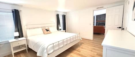 A bedroom with a bed, bedside tables, and a nightstand. There is a door leading to a bathroom.