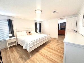 A bedroom with a bed, bedside tables, and a nightstand. There is a door leading to a bathroom. - The Blue Pony - 5 Miles to WEC! 10 Miles to HITS! (Ocala)
