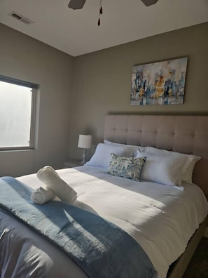 Ein Hotelzimmer mit Bett, Fenster, einem Bild an der Wand und einer Nachttischlampe.