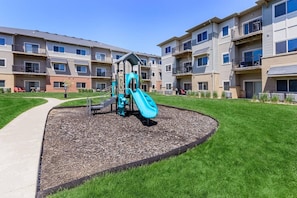 Ein Spielplatz mit Rutsche und Klettergerüst, umgeben von einer angelegten Grünfläche mit einem Weg.