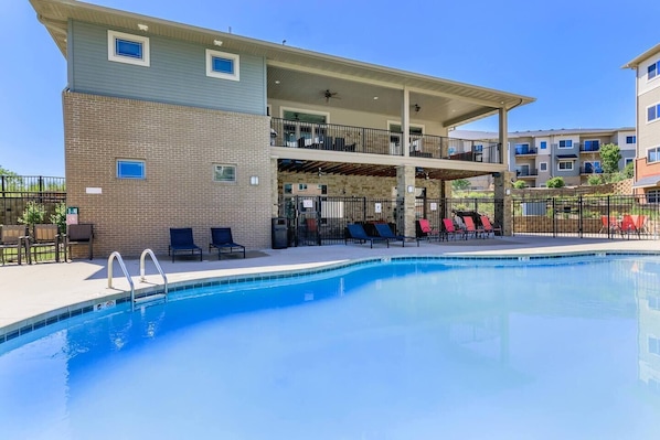 Ein Pool mit Liegestühlen, eine überdachte Terrasse und ein mehrstöckiges Gebäude mit Balkonen.